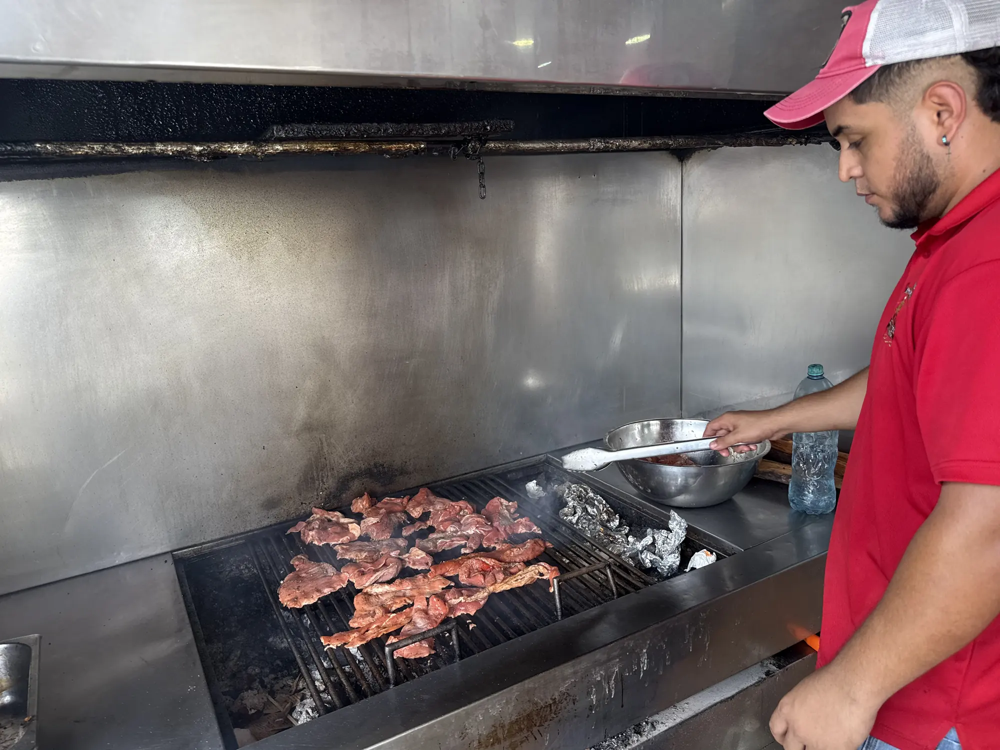Parrillero volteando carne sobre la parrilla de carbón de El Rancho Interiorano