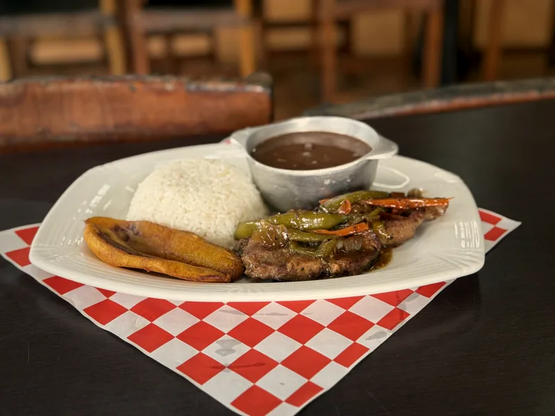 Bistec encebollado con arroz blanco, frijoles y tajadas