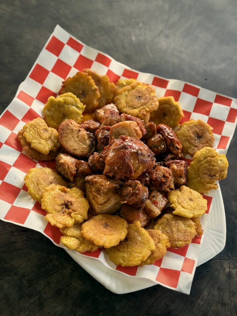 Picada de ahumados con salsa BBQ y patacones sobre papel a cuadros, vista desde arriba