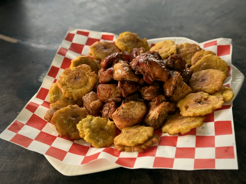 Picada de ahumados con salsa BBQ y patacones sobre papel a cuadros, en la terraza