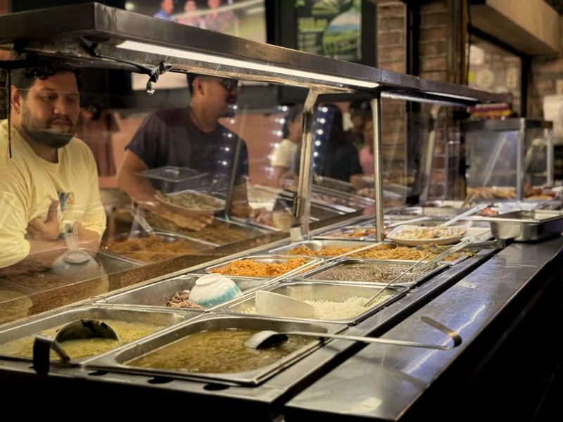 El cocinero detrás de la vitrina caliente con las bandejas del día